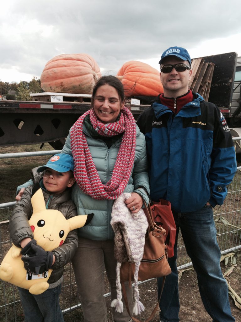 Family poses by large truck with giant pumpkins