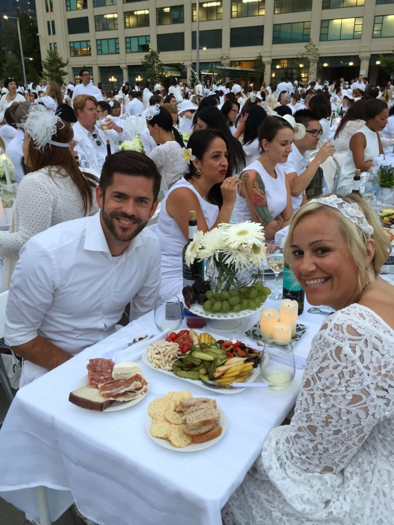 Couple at Diner en Blanc table, dressed in white, surrounded by other couples in white