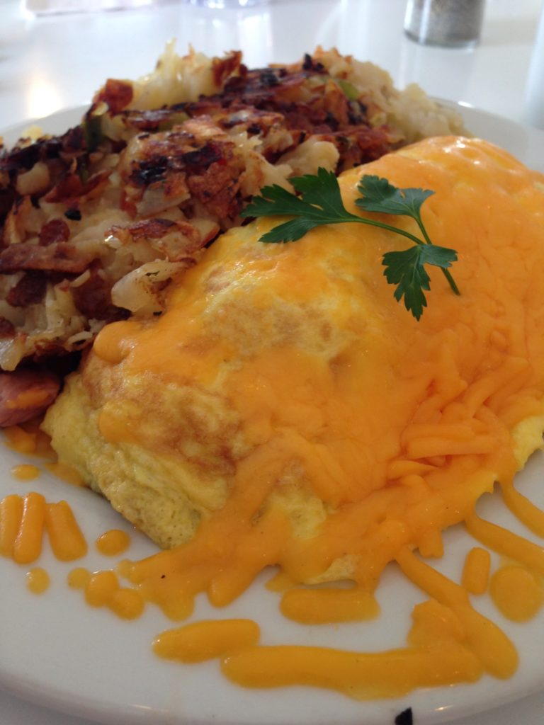 omelette covered in melted cheese, with hash browns on a plate for comfort food in Long Beach