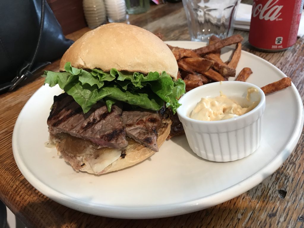 Rib-eye steak sandwich with sweet potato fries and dip during lunch in Orangeville