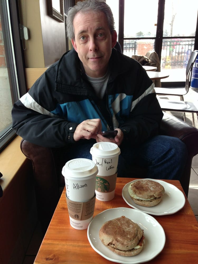 man sits at a table with  2 coffees and 2 breakfast sandwiches at Starbucks drive-thru in Ajax
