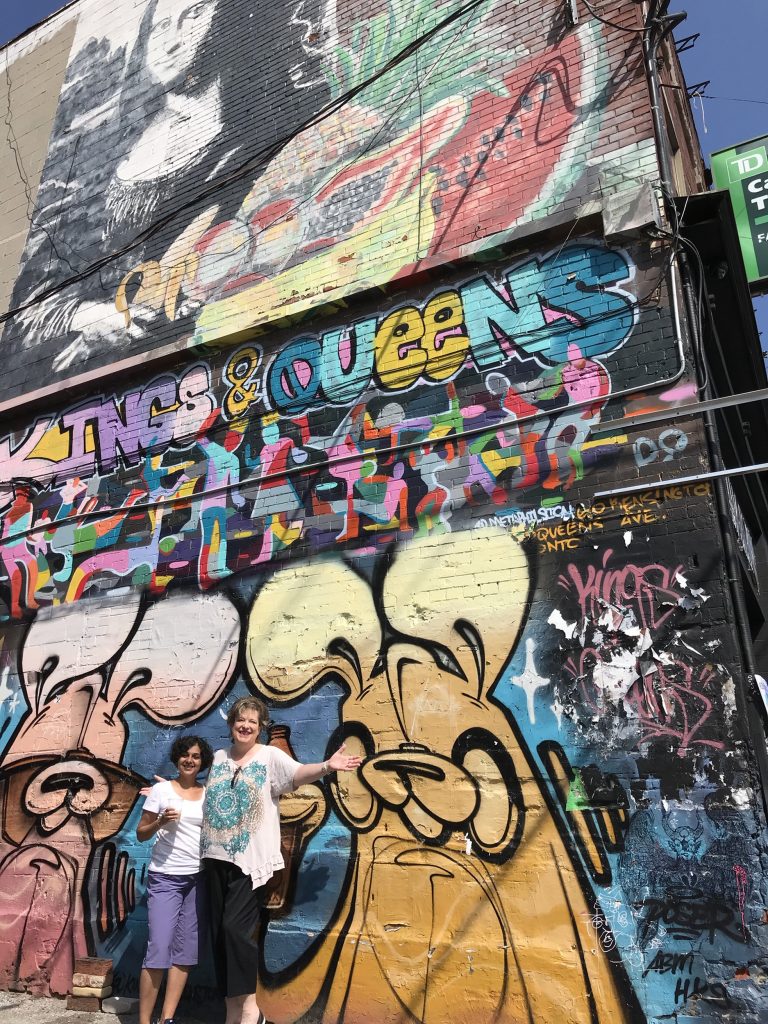 Hema and Allison pose by street art wall